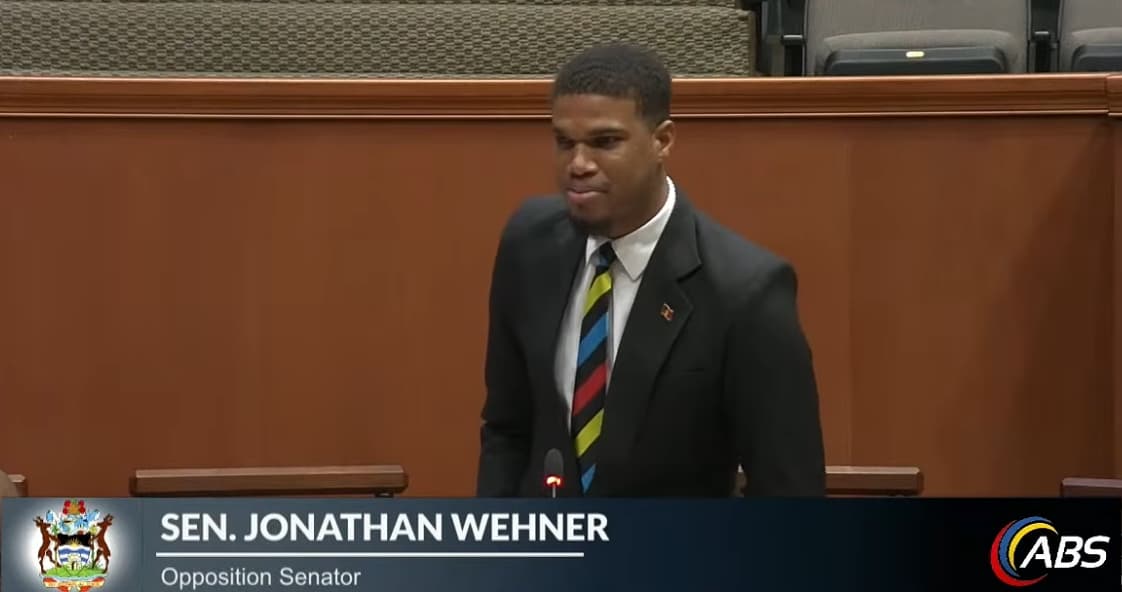 jonathan wehner talking in parliament in antigua tie and black suit looking at top of government bench intently